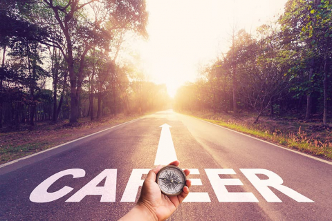 Hand holding compass on empty asphalt road with the word 'Career' written on the road.