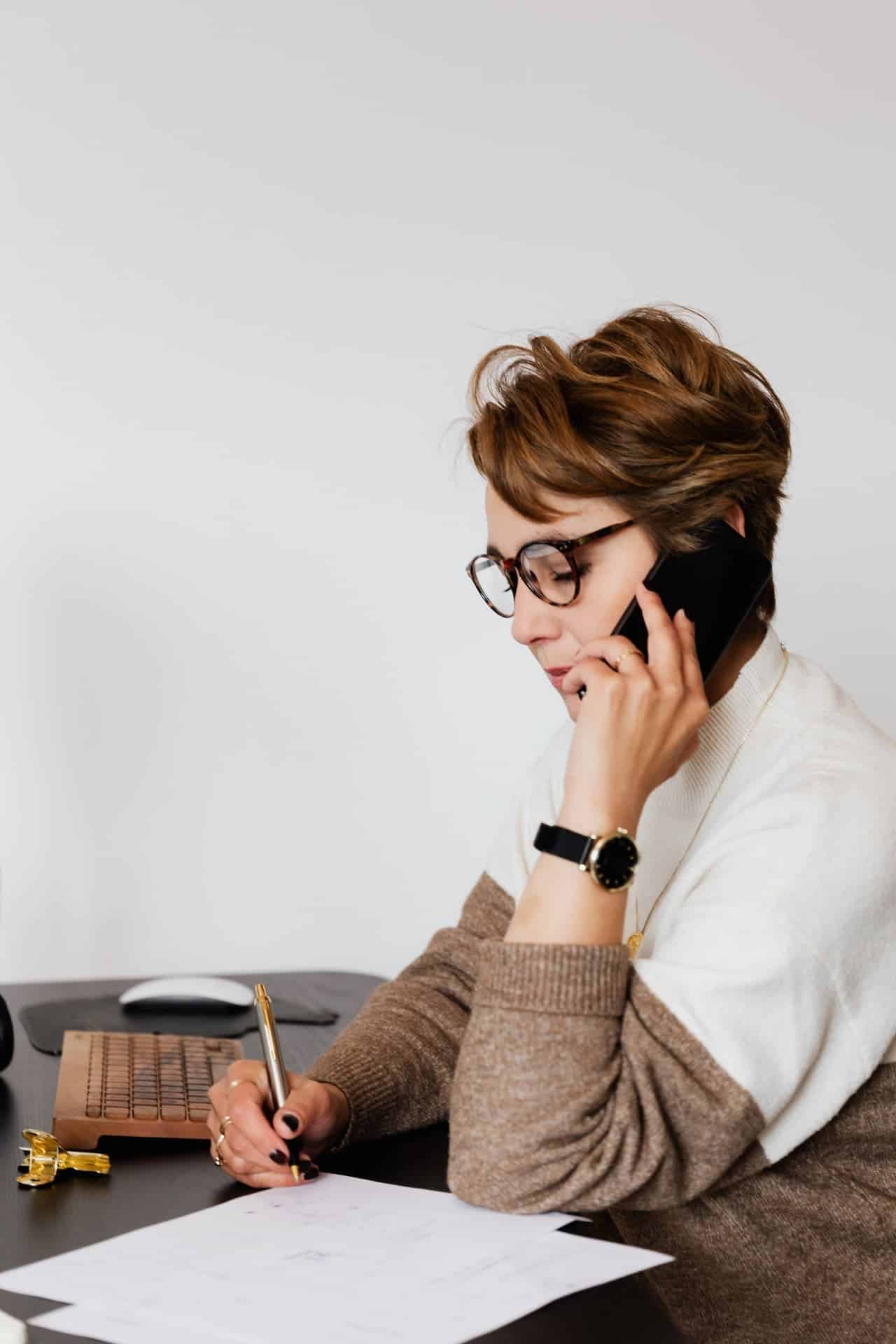 businesswoman speaking on smartphone and writing on paper in office