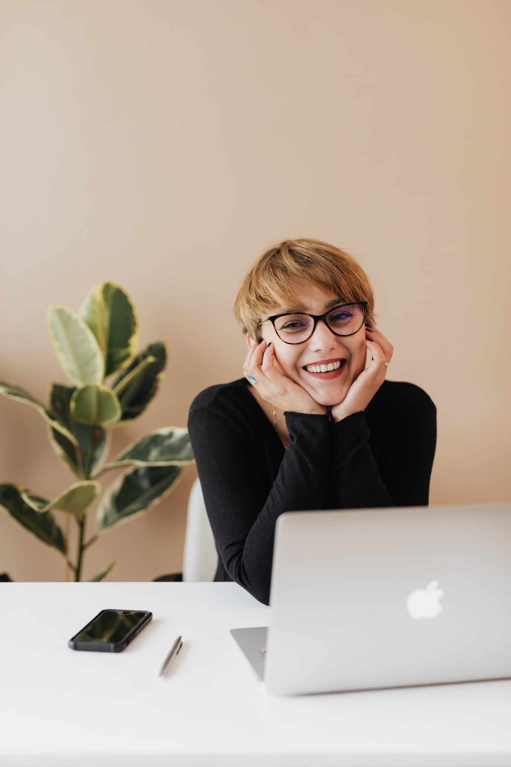 Cheerful woman smiling while sitting at table with laptop.