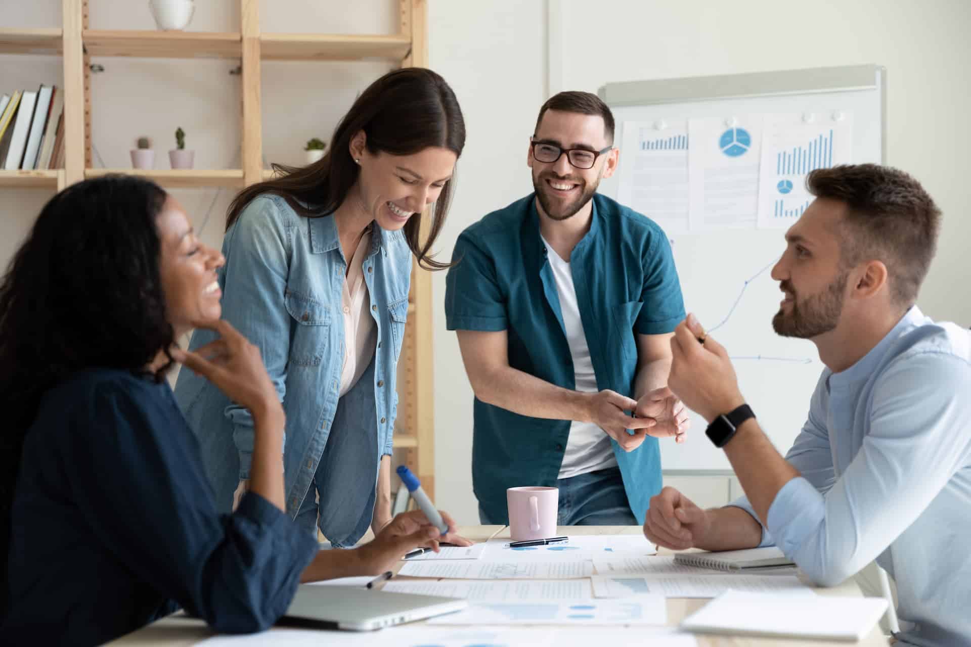 Smiling diverse colleagues gather in boardroom brainstorm discuss financial statistics together, happy multiracial coworkers have fun cooperating working together at office meeting.