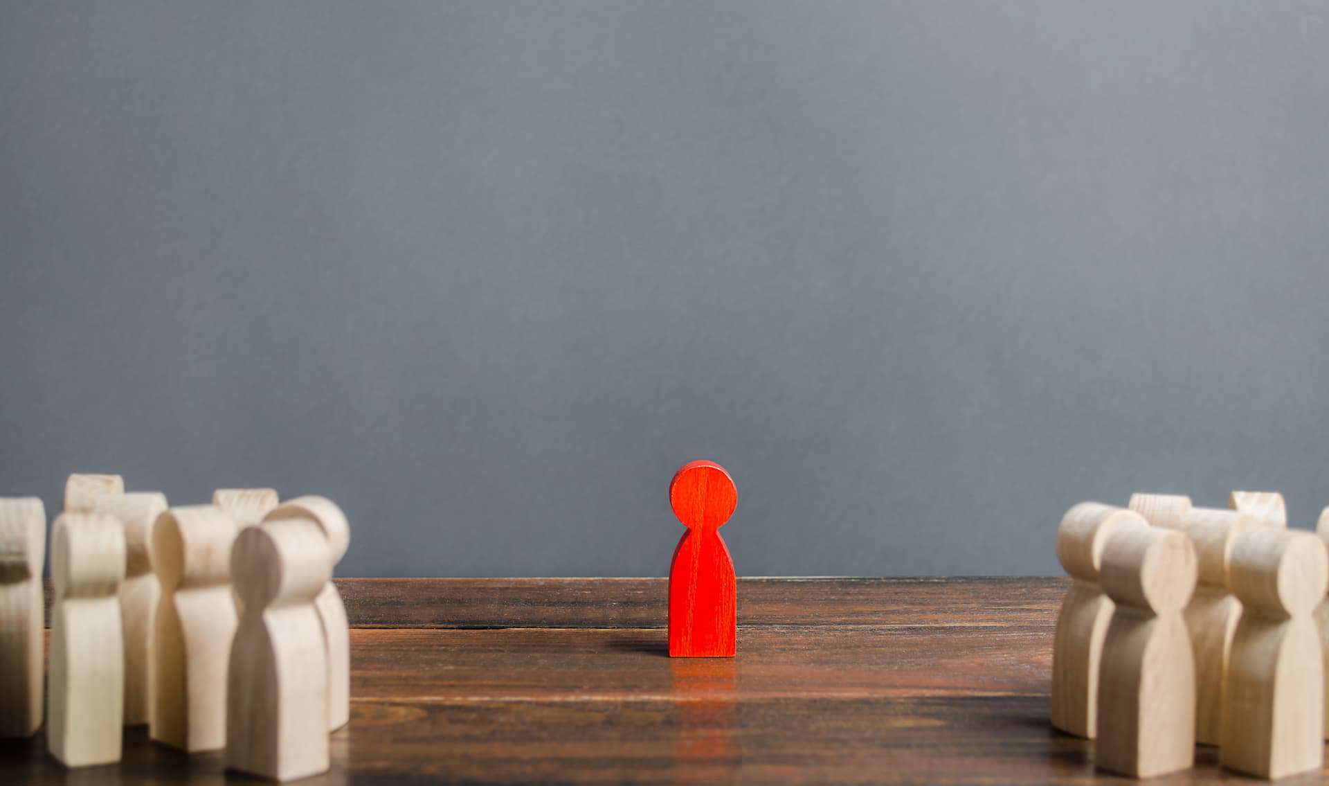 Red wooden figurine of a man stands aside from the crowd of wood figurine people.