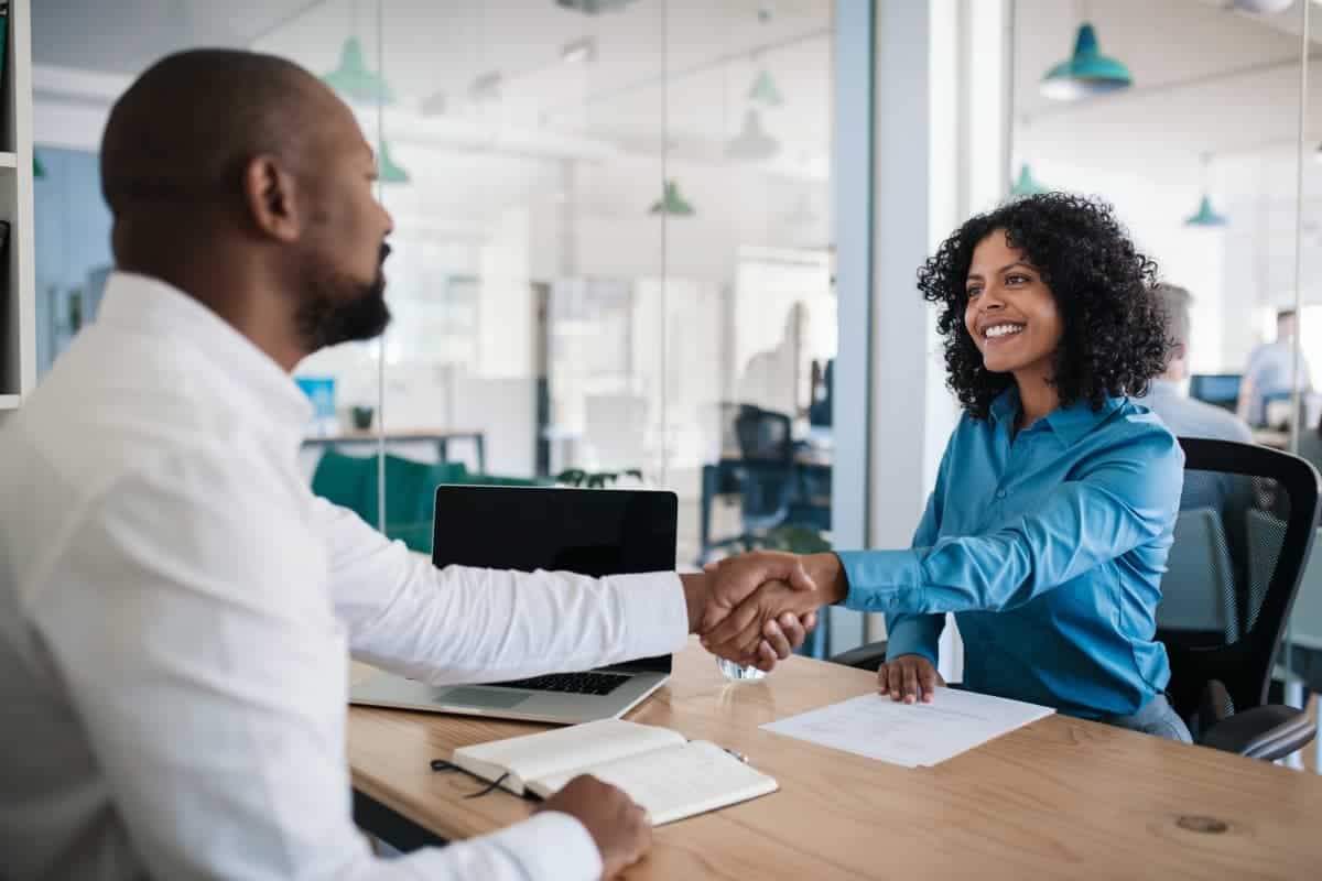 Happy young woman shaking hands with a hiring manager in an office setting.