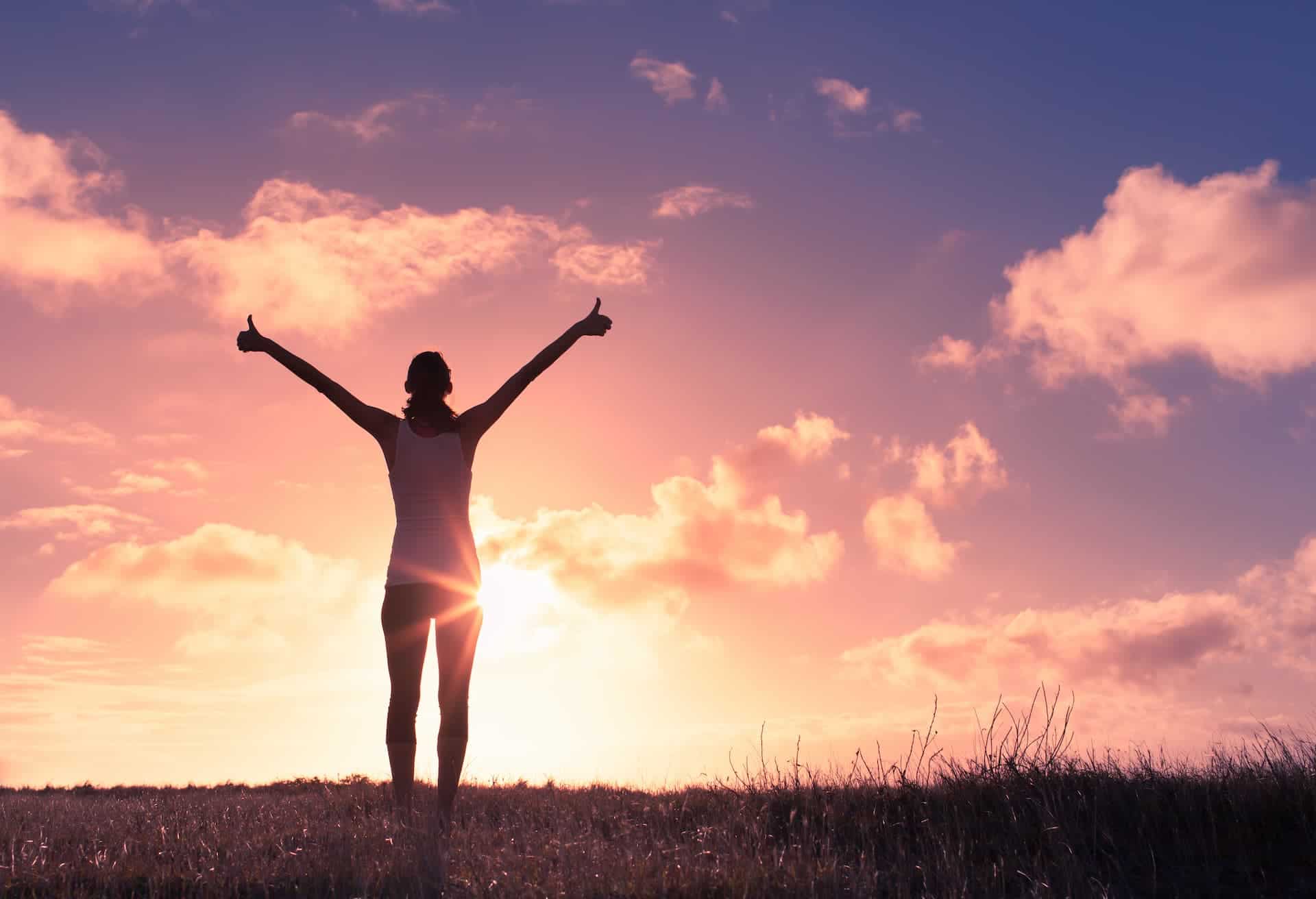 Silhouette of joyful woman outdoors at sunset with her hands in the sky.