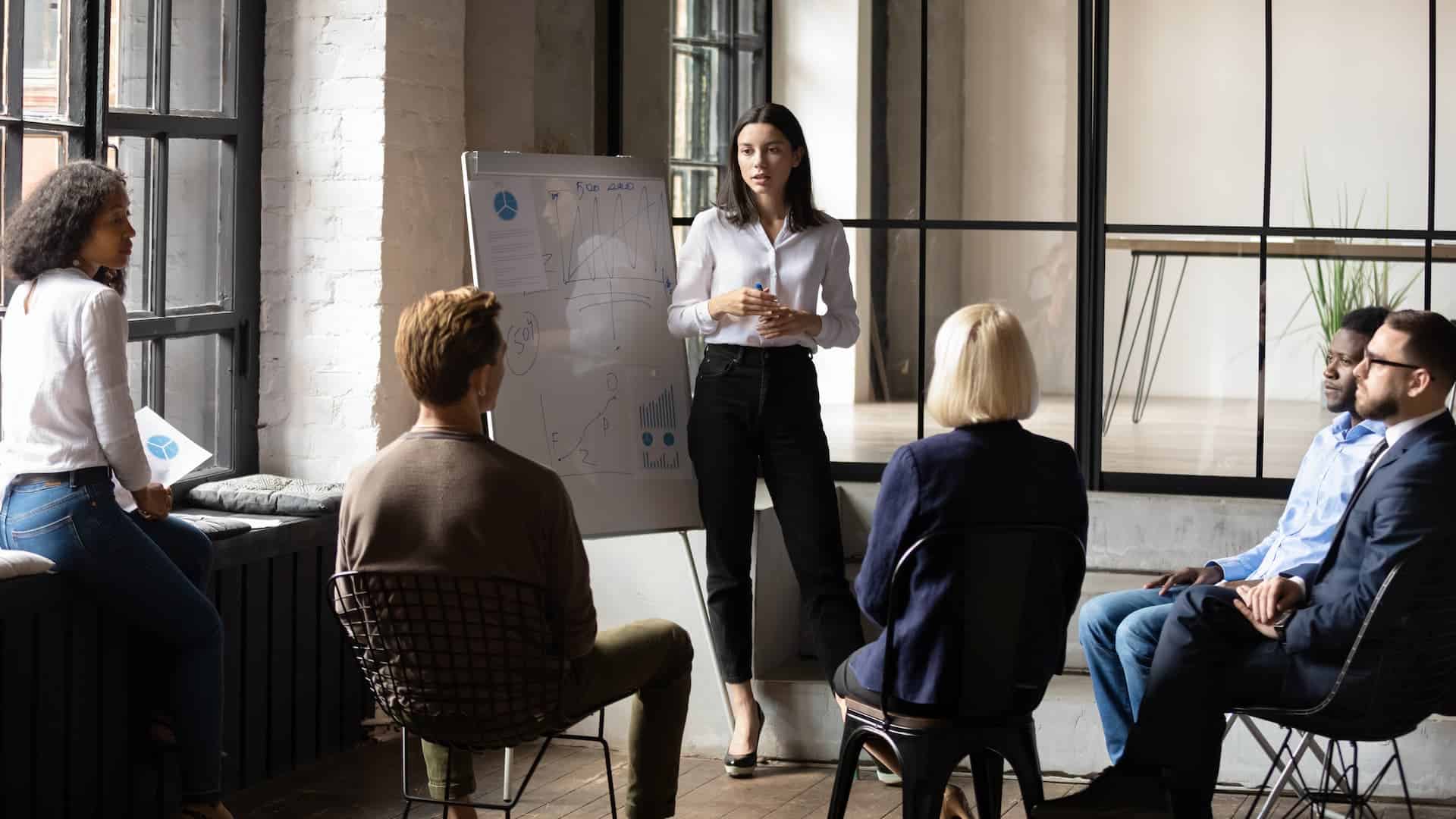 Confident lady business woman standing by a whiteboard leading a meeting.