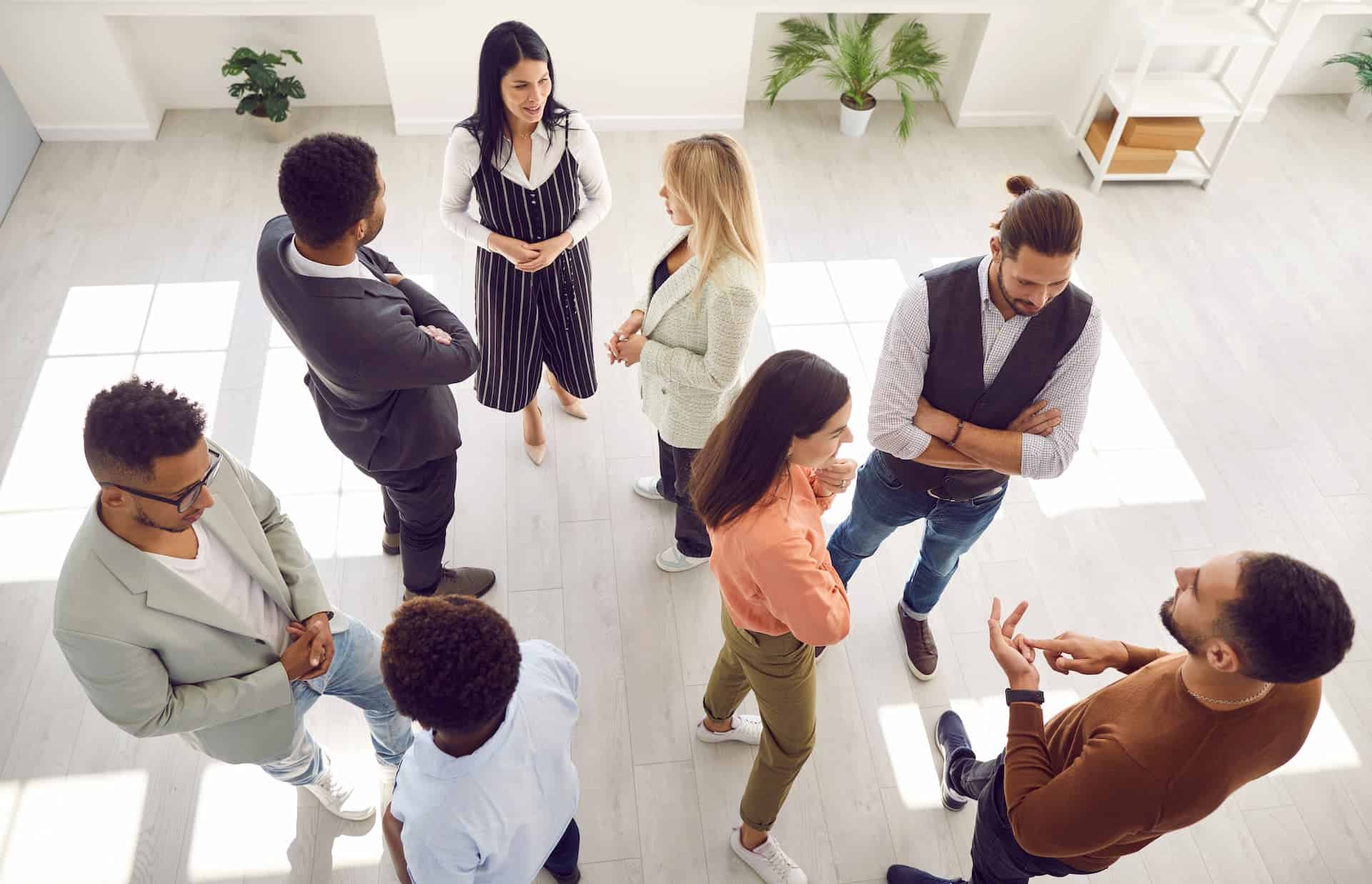 Bird's eye view of diverse men and women standing in office talking with each other.